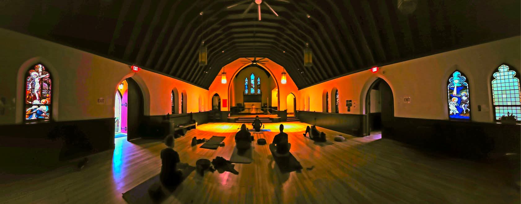 People practice yoga in the Manitou Springs Commons’ historic hall with stained-glass windows and warm ambient lighting.
